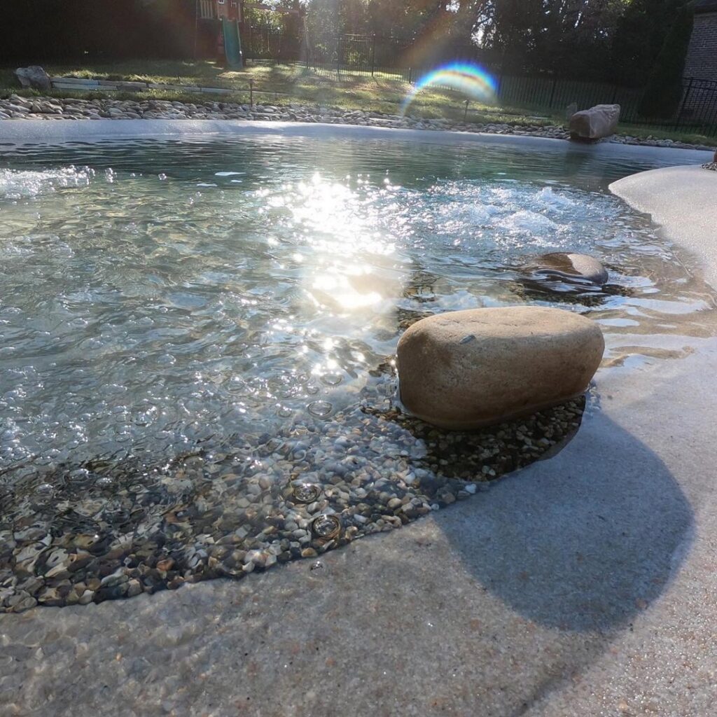 A close-up of a pool edge with a bubbling water feature and decorative pebble detail, installed by The Staycation Builders in Fort Wayne, IN.