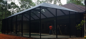 A pool enclosure under construction with a pool visible inside by Backyard Paradise in Mobile, AL.