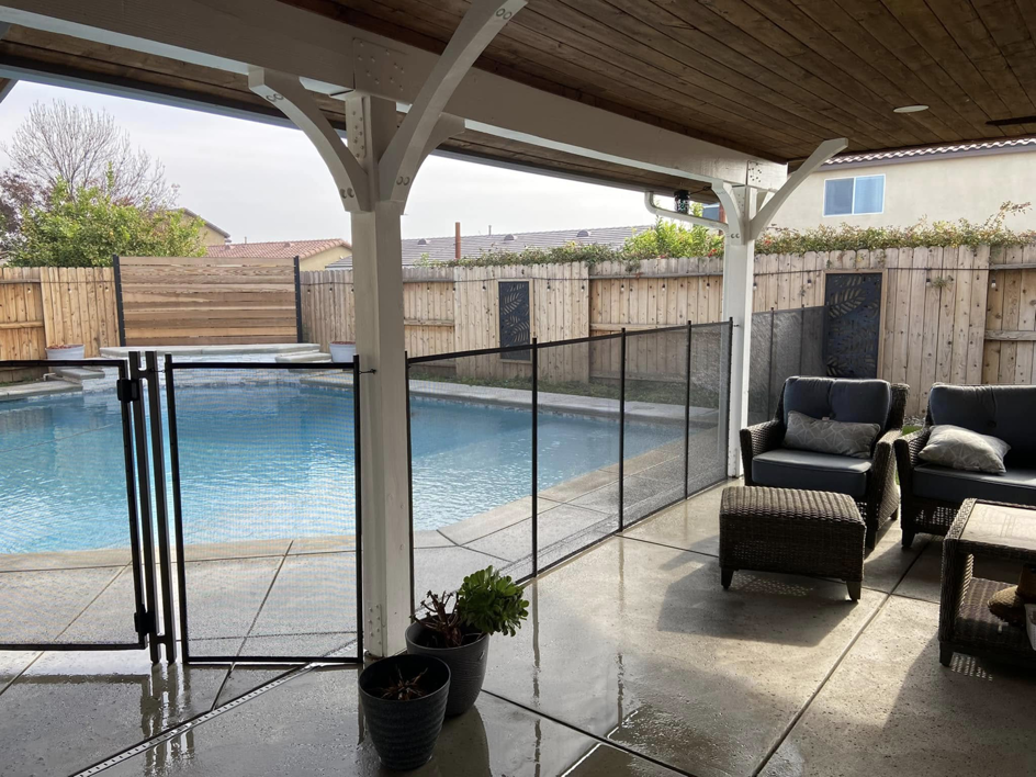 A black mesh pool fence featuring a self-closing gate, installed under a patio by A Safe Pool Enclosures in Bakersfield, CA.