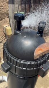 A pool filter backwashing, with water spraying out, demonstrating maintenance by Good Guy Pool Service in Moreno Valley, CA.