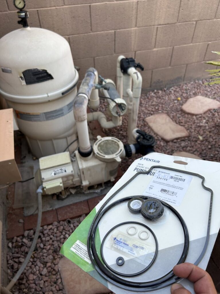 A hand holding pool pump repair parts in front of a pool equipment system by Classic Pool Service in Surprise, AZ