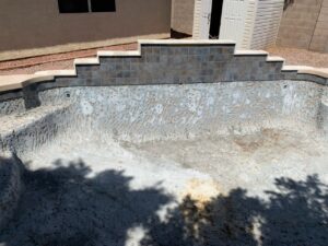 An empty pool during renovation, showing new tile work on the waterfall feature by East Mesa Pools, LLC in Mesa, AZ.