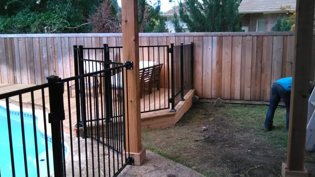 A newly installed black metal pool safety fence and wooden privacy fence by Dallas Mobile Welder, LLC. in Dallas, TX.