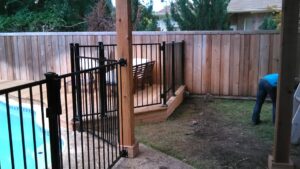 A newly installed black metal pool safety fence and wooden privacy fence by Dallas Mobile Welder, LLC. in Dallas, TX.