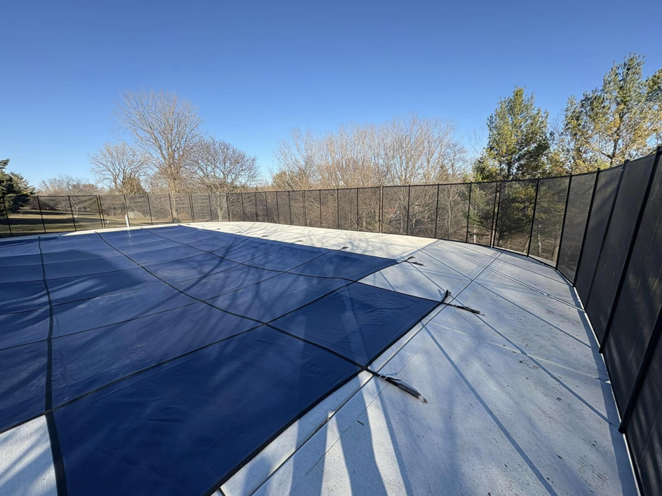 An installed black mesh pool safety fence enclosing a pool with a blue cover by Safe Yard Fence - Waukesha County in Waukesha, WI.