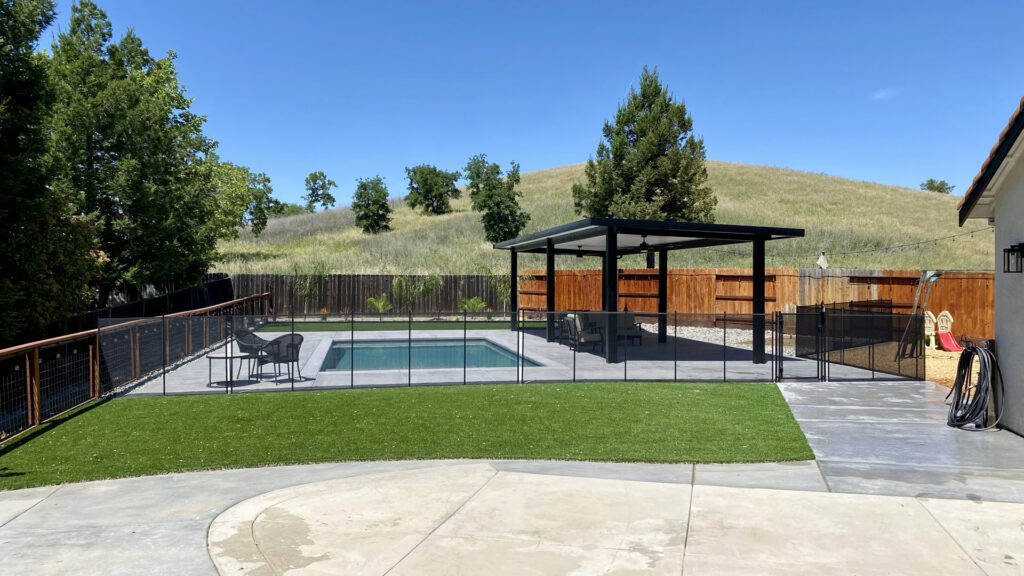 A modern backyard pool featuring a black mesh safety fence and gate installed by Golden State Baby Barrier in Sacramento, CA.