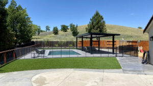 A modern backyard pool featuring a black mesh safety fence and gate installed by Golden State Baby Barrier in Sacramento, CA.