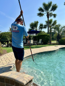 A Freedom Pools service technician in a blue shirt actively skimming a clean swimming pool in Austin, TX.