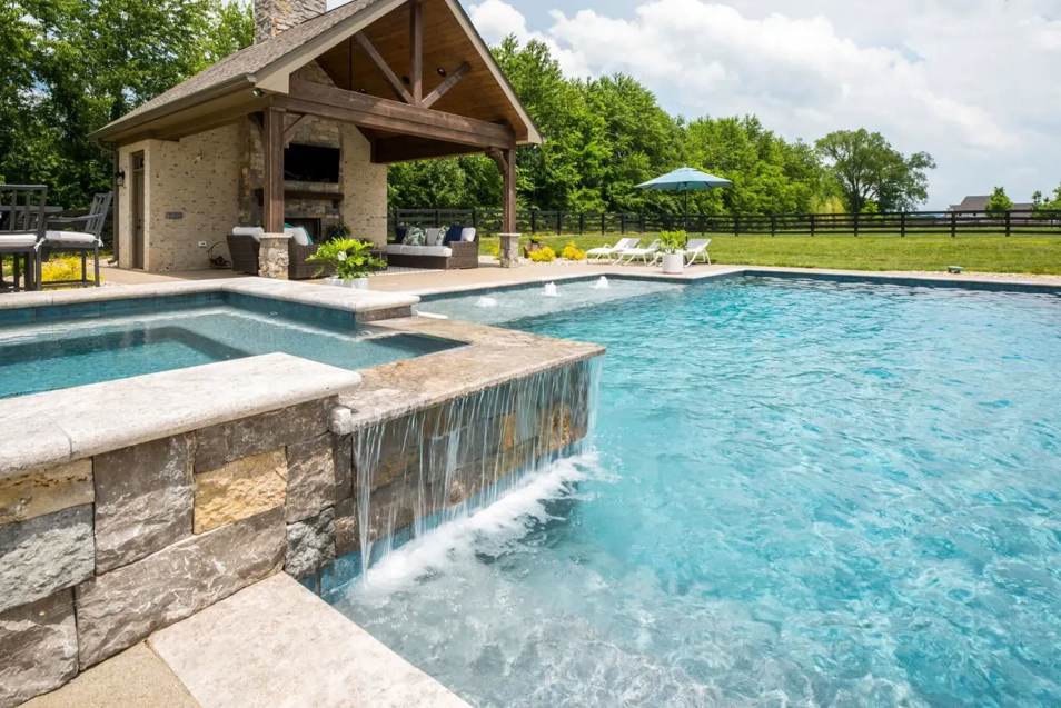 A swimming pool with an attached spa and waterfall feature next to a pool house by Top Tier Pools in Franklin, TN.