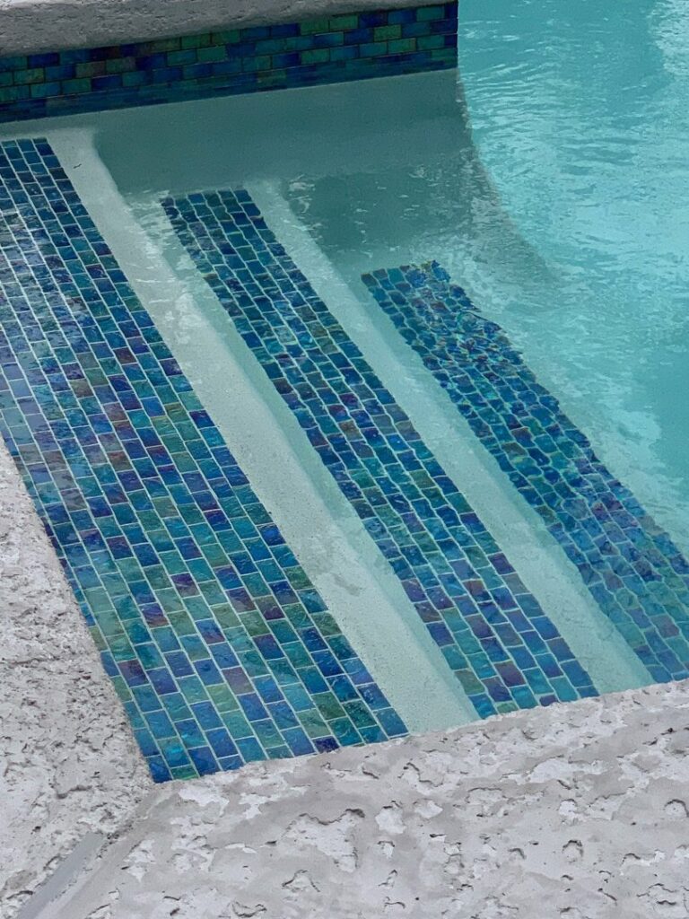 Close-up of swimming pool steps adorned with vibrant blue mosaic tiles, showcasing work by I10 Pool Plastering LLC in Kenner, LA.