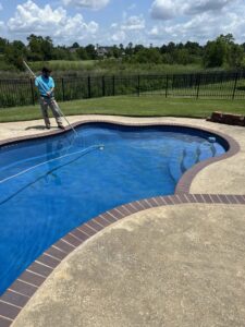 A pool technician from Gayle Force Pools performing routine cleaning on a residential pool in Lake Charles, LA