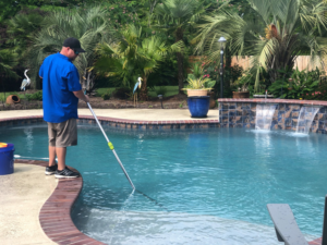 A pool technician from Brocks Pools LLC skimming leaves and debris from a residential pool in Baton Rouge, LA.