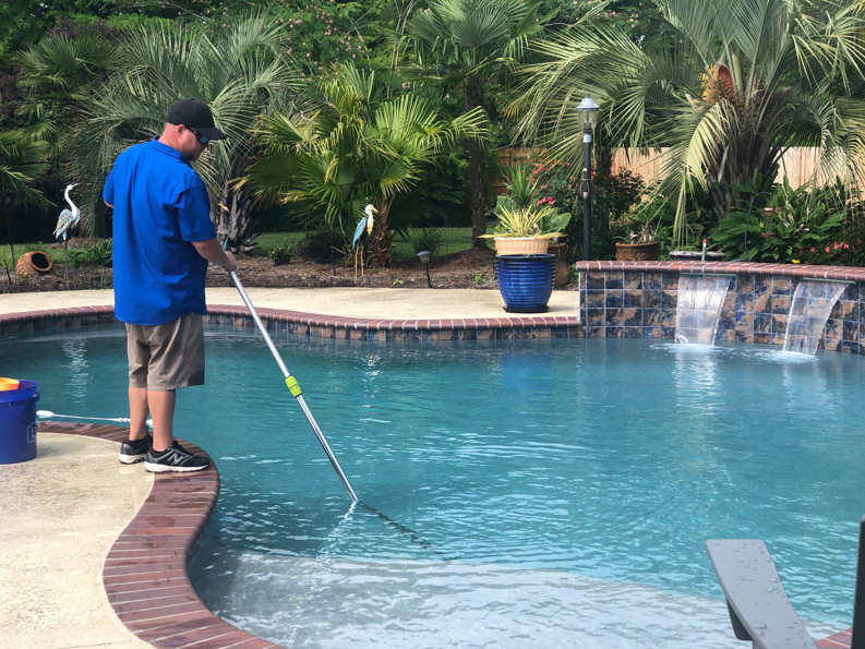 A pool technician from Brocks Pools LLC skimming leaves and debris from a residential pool in Baton Rouge, LA.