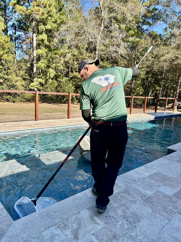 A pool technician from Freedom Pools skimming leaves and debris from a swimming pool in Austin, TX.