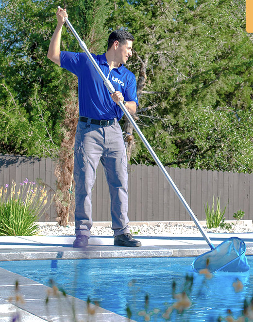 A pool technician using a long-handled net to skim debris from a pool for Ultra Pool Care Squad of East Chattanooga, TN.