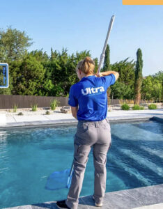 A pool technician skimming leaves from a pool with a net for Ultra Pool Care Squad of East Chattanooga, TN.