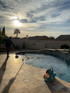 A pool technician skimming the water during a cleaning service by Parkinson Pools in Peoria, AZ