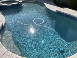 A pool vacuum hose actively cleaning a sparkling residential pool, showcasing services by Orona Pool Care LLC in Mesa, AZ.