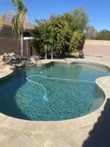 A pool vacuum cleaning a sparkling blue swimming pool, demonstrating service by BEHR POOLS Service & Repairs in Glendale, AZ