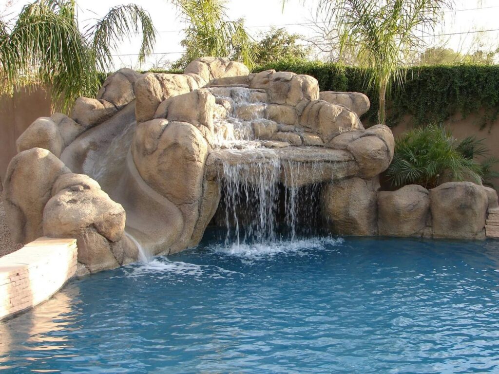 A swimming pool featuring a large rock waterfall and slide, built by Blue Magic Pools and More Inc. in Gilbert, AZ.