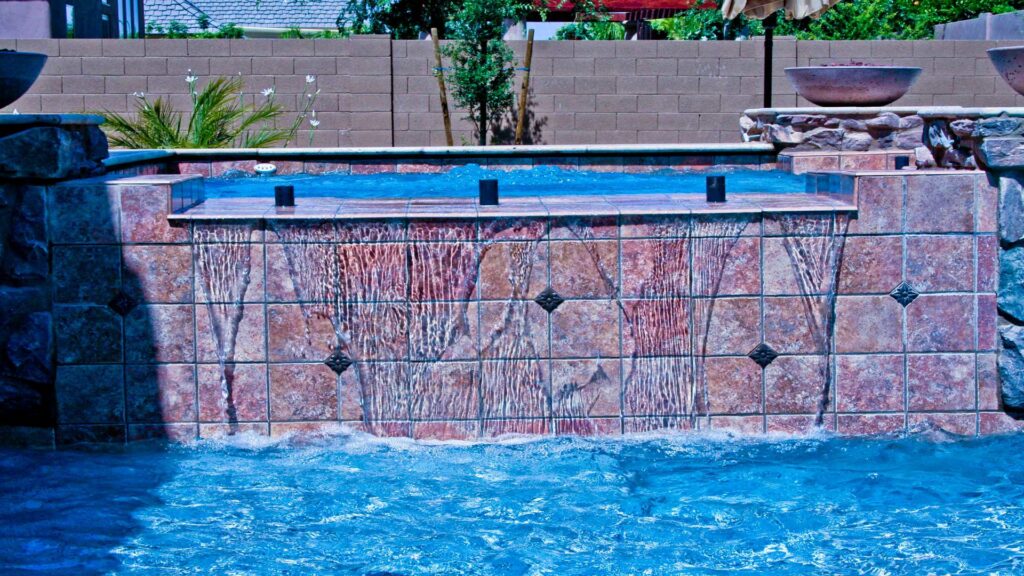 A swimming pool with a decorative tiled water wall feature by Blue Magic Pools and More Inc. in Gilbert, AZ.