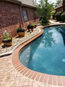 Beautiful poolside landscaping with decorative pebbles and potted plants by GAMAS Lawn Care Services in Tulsa, OK.