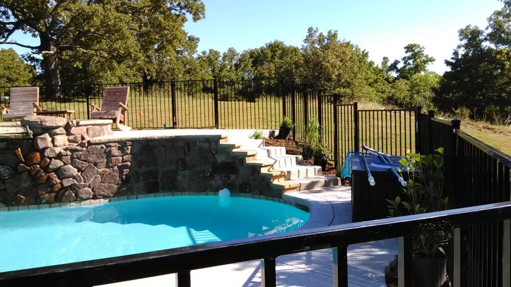 A black metal fence installed around a poolside area with stone steps by Dallas Mobile Welder, LLC. in Dallas, TX.
