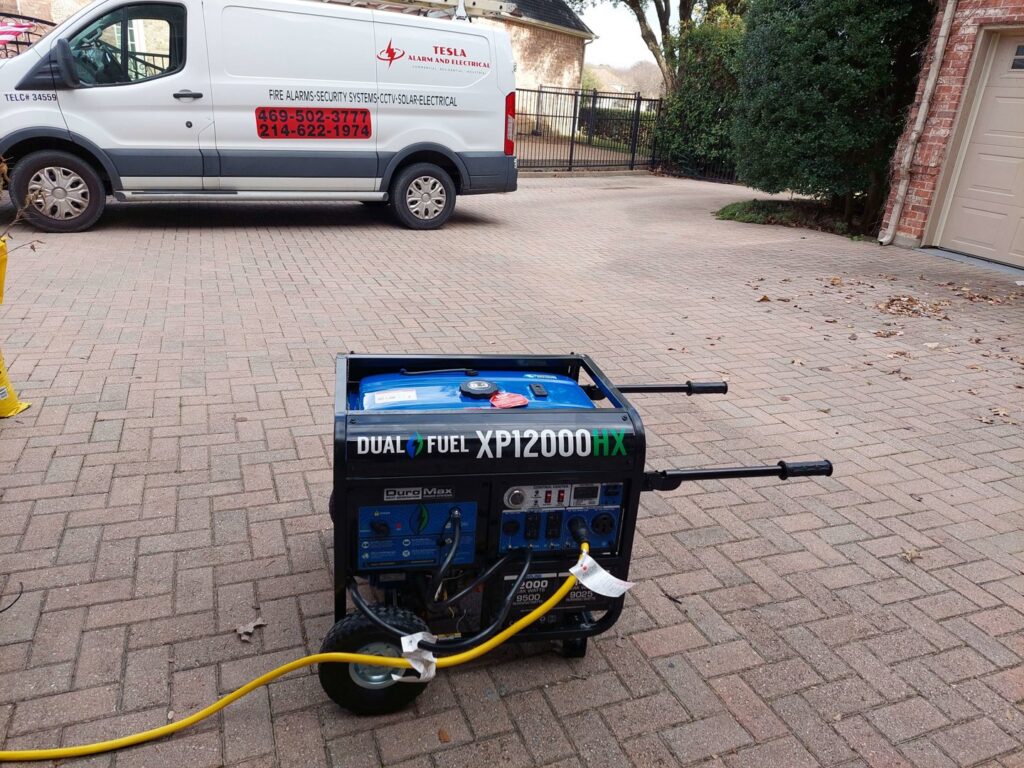 A portable generator connected with a yellow cable, next to a Tesla Alarm and Electrical service van in Plano, TX