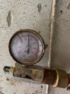 A close-up of a rusty pressure gauge being inspected on an HVAC or heating system by Alan Energy Services in Naperville, IL