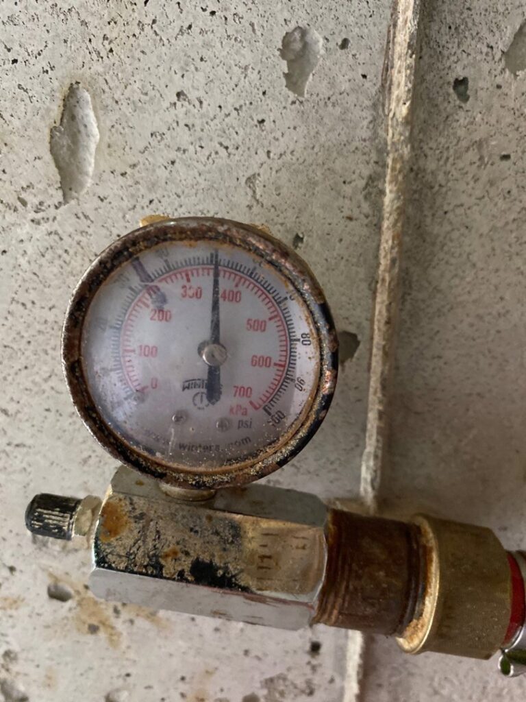 A close-up of a rusty pressure gauge being inspected on an HVAC or heating system by Alan Energy Services in Naperville, IL