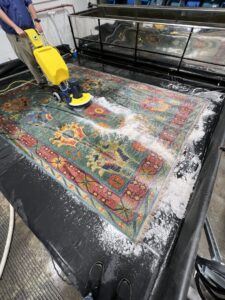 A professional using a rotary scrubber to clean a large area rug in a dedicated facility for Hydro Clean in Baltimore, MD.