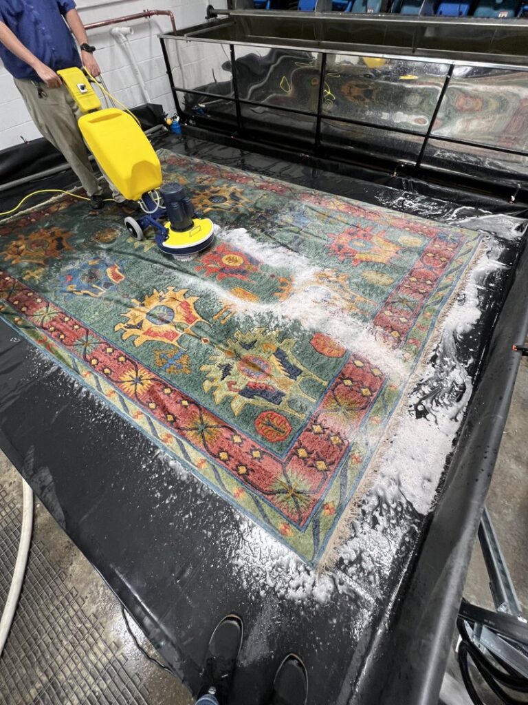 A professional using a rotary scrubber to clean a large area rug in a dedicated facility for Hydro Clean in Baltimore, MD.