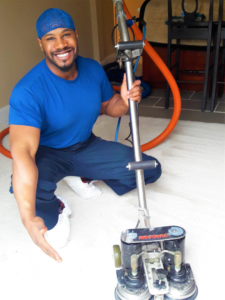 A professional carpet cleaner with a Rotovac machine smiling and gesturing to a freshly cleaned carpet by Maxcarp Carpet Cleaning in Kent, WA.
