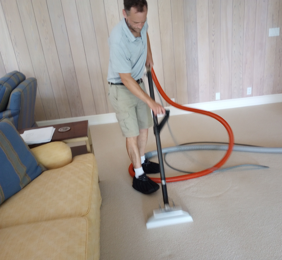 A professional carpet cleaner using a wand to clean a light-colored carpet in a living room by All Heart Carpet Cleaning in Eugene, OR.