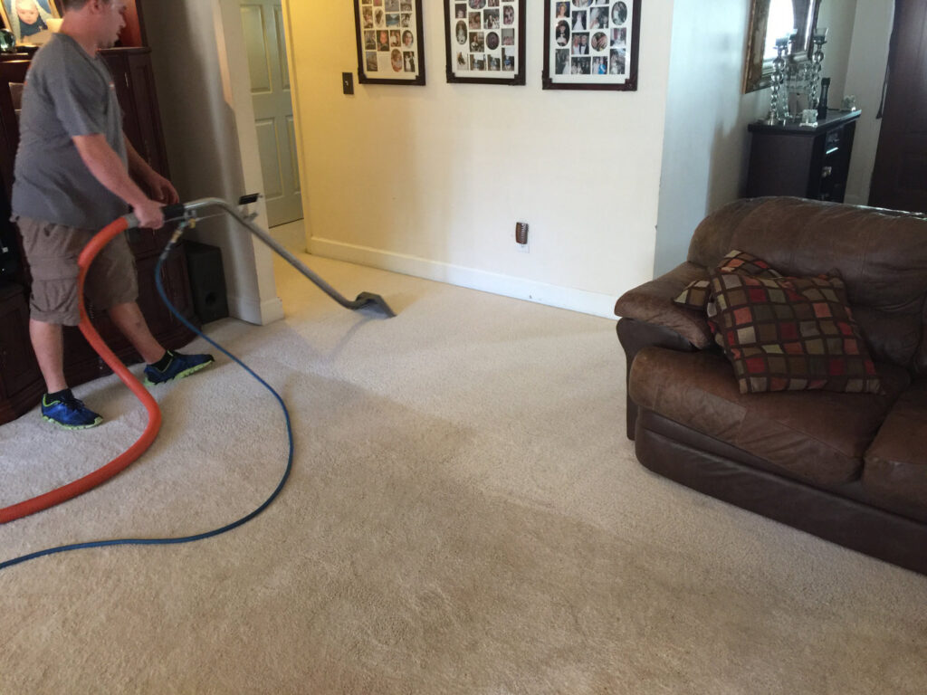 A professional cleaning a light-colored carpet in a living room, showing the cleaned area, by Xtreme Klene Carpet & Upholstery Cleaning in Montgomery, AL.
