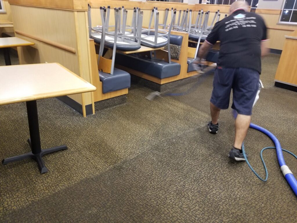 A professional cleaning a brown carpet, showing a clean strip, wearing blue shoe covers, by New Dawn's Carpet Cleaning in Cicero, IL.