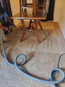 A professional performing carpet cleaning under furniture, showing clean results, by Spot On Carpet Cleaning of Columbia, SC.