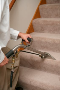 A professional cleaning technician deep cleaning carpeted stairs with specialized equipment from Upholstery Cleaning Services in Los Angeles, CA.