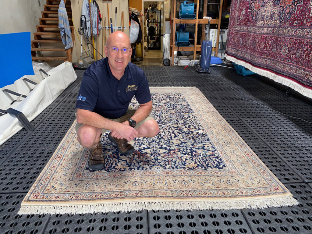 A professional from Rug Renew kneeling beside a beautiful patterned rug, likely for inspection or presentation in Spring Valley, CA.