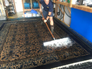 A professional from Rug Renew meticulously scrubbing a large patterned rug with a brush and cleaning solution in Spring Valley, CA.