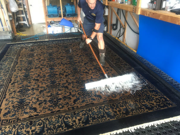 A professional from Rug Renew meticulously scrubbing a large patterned rug with a brush and cleaning solution in Spring Valley, CA.