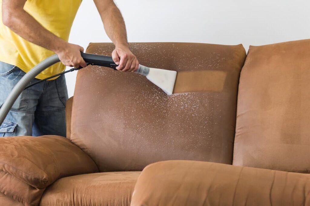 A professional cleaning a brown sofa with an upholstery cleaning tool for Nashville Carpet Cleaning in Madison, TN.