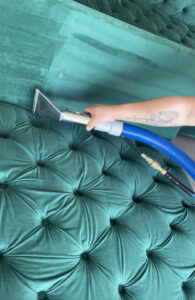 A professional performing upholstery cleaning on a green tufted sofa with a specialized tool by Good Guys Carpet Cleaning in Katy, TX.