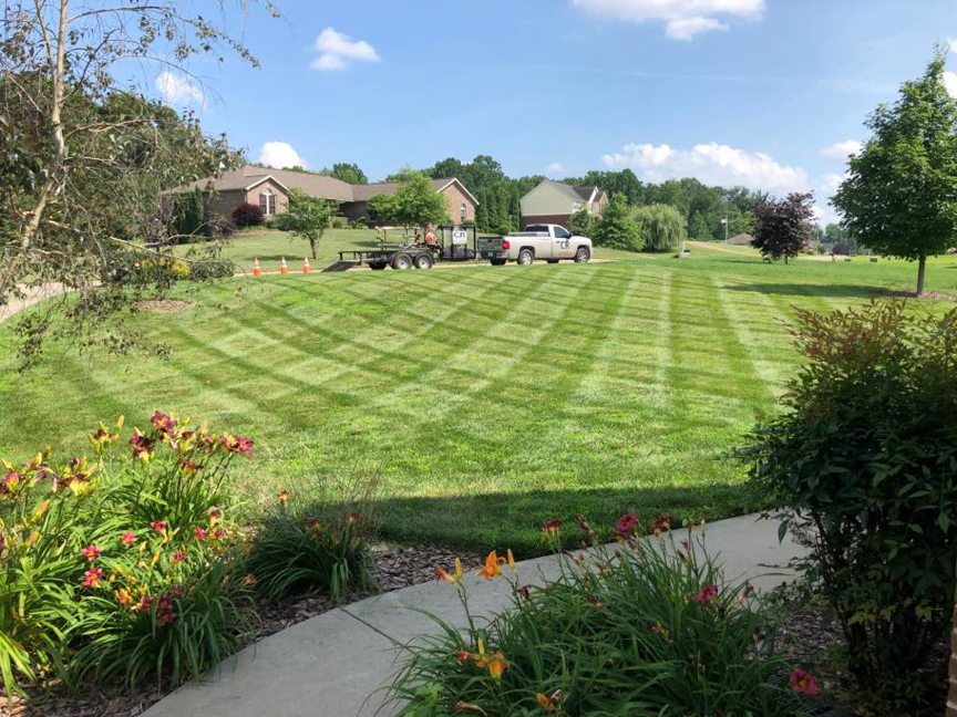 A beautifully mowed lawn with a crisscross pattern, showing a C&R Lawn Care and Property Services truck and trailer in Evansville, IN.