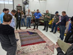 Professionals gathered around a large area rug, inspecting it at the Association of Rug Care Specialists in Salem, OR