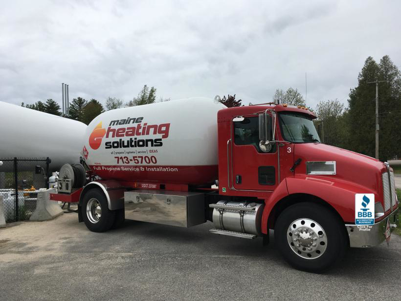 A red Maine Heating Solutions propane delivery truck next to a large tank in South Portland, ME.