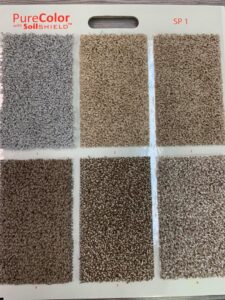 A display board featuring "PureColor with SoilSHIELD" carpet samples in various shades, offered by Rojas Carpet and Flooring in Denver, CO.