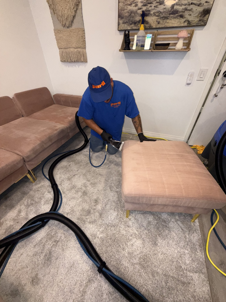 A Purli technician cleaning an ottoman with professional equipment in a client's home in San Diego, CA.