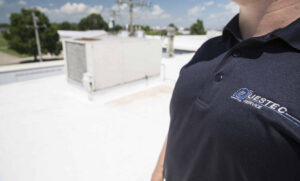 A QuesTec HVAC service technician wearing a branded uniform with a rooftop HVAC unit in the background in Columbia, MO