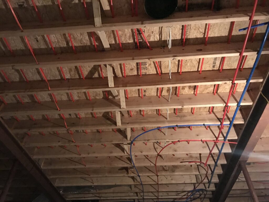 Red and blue radiant floor heating pipes installed within a wooden floor joist system by Simply Installs Heating & Air Conditioning in Shortsville, NY.